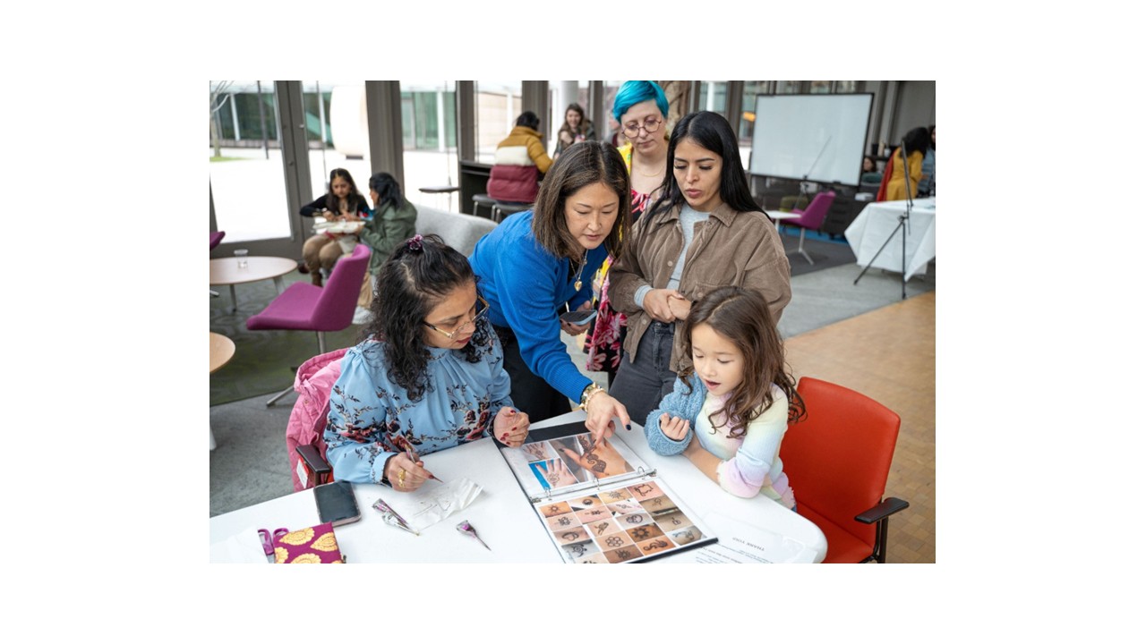 Employees and a child looking through a henna design portfolio at a corporate event