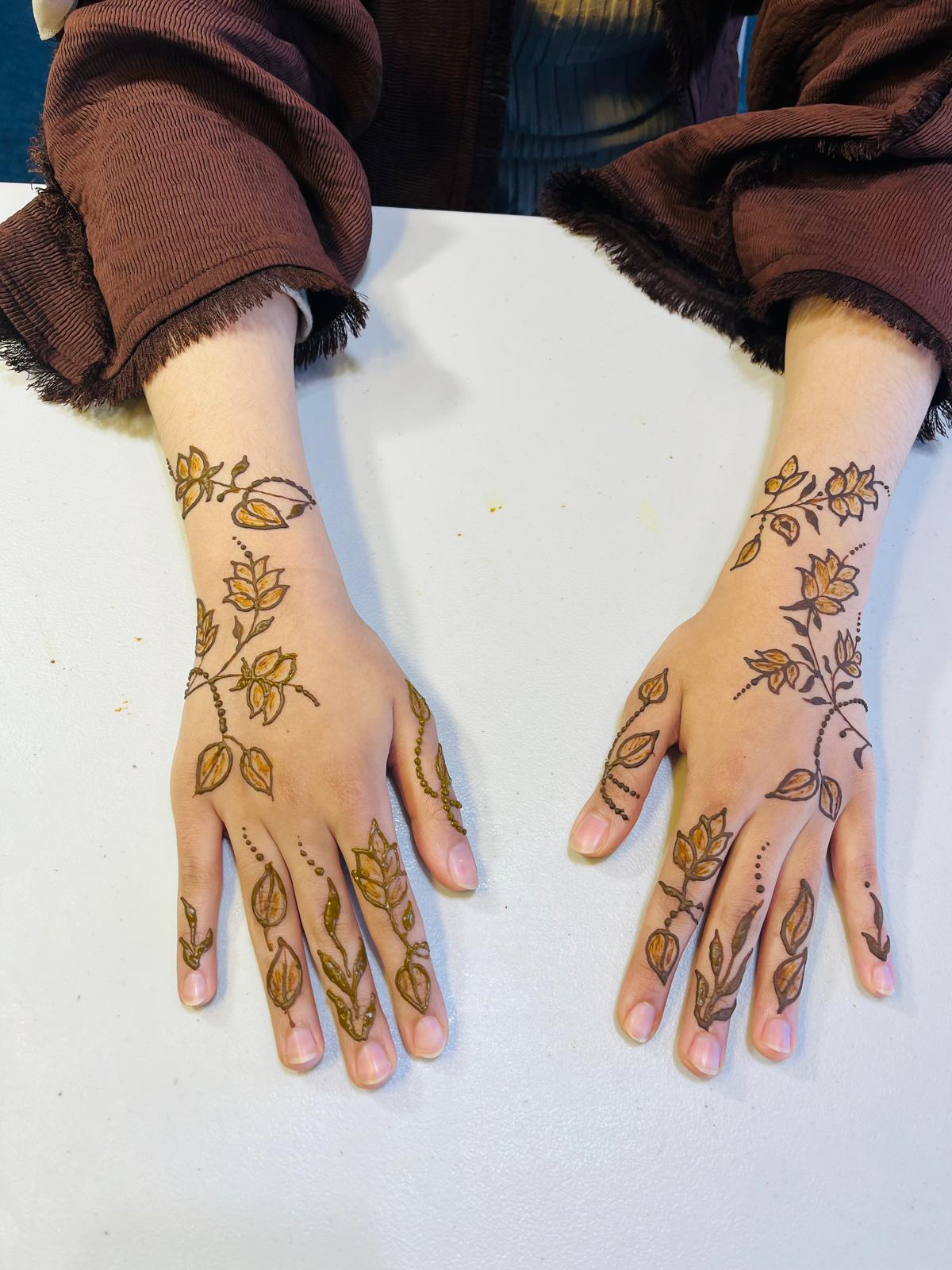 Two hands with intricate black Arabic-style floral henna
