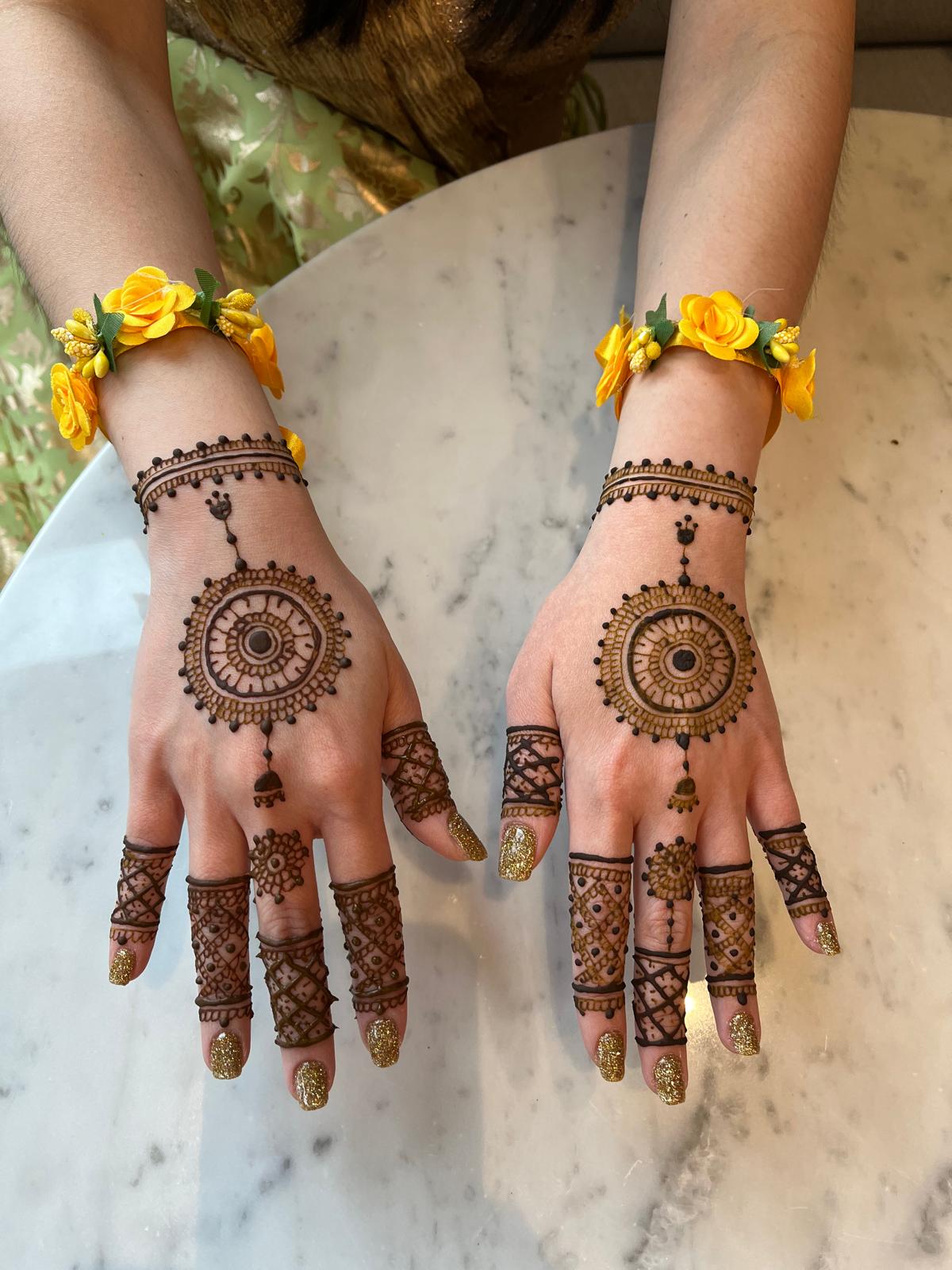 Matching mandala henna on both hands with beaded finger designs at a festival
